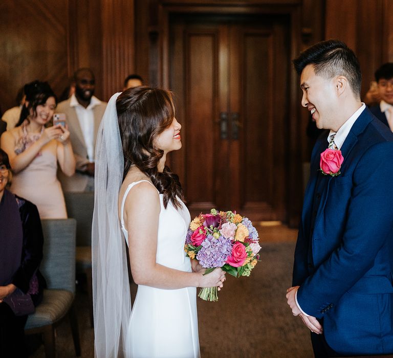 Bride holds colourful bouquet whilst stood with her groom at The Old Marylebone Town Hall