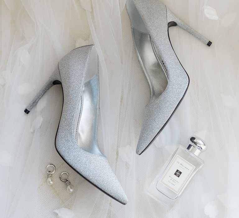 Silver glitter heeled bridal shoes beside pearl earrings and Jo Malone perfume 