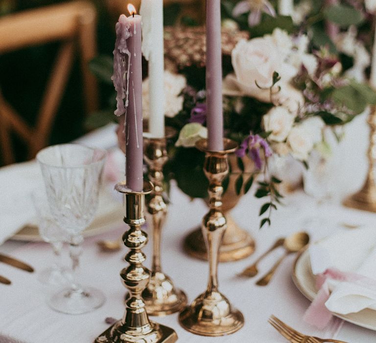 White and lavender tapered candles in gold candle holders on neutral wedding tablescape with gold accents