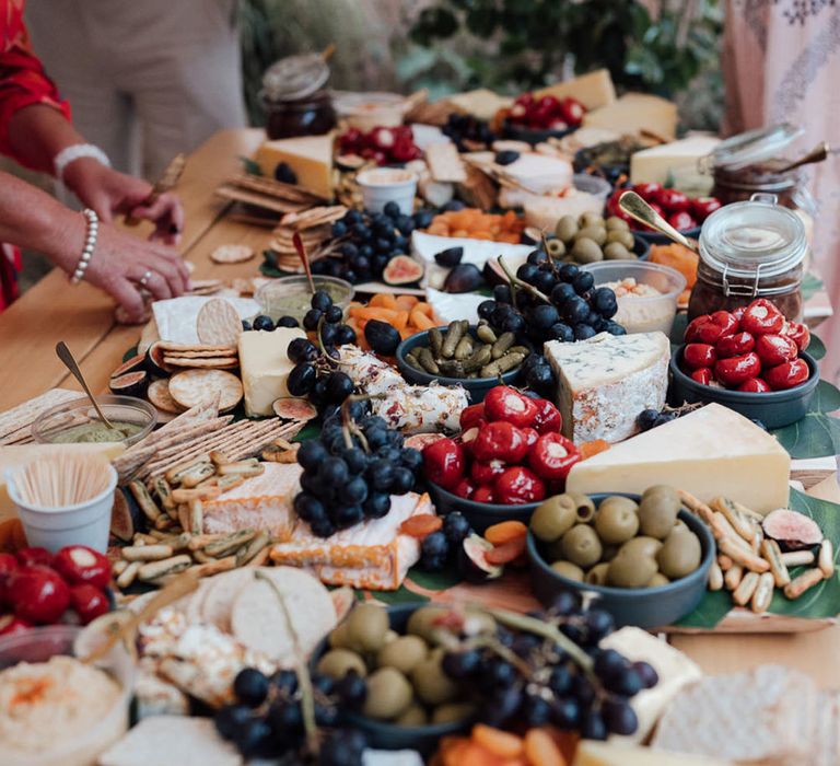 Grazing table with cheeses, crackers, grapes, dried fruits, olives, gherkins, and stuffed peppers 