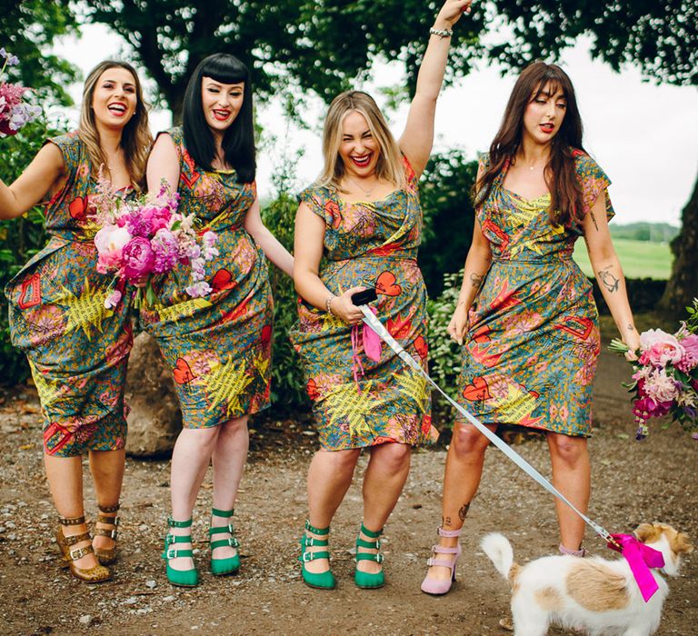 Bridesmaids in matching midi green colourful patterned Vivienne Westwood bridesmaid dresses with ruching, short sleeves and mismatched colour three strap shoes holding pink floral bouquets