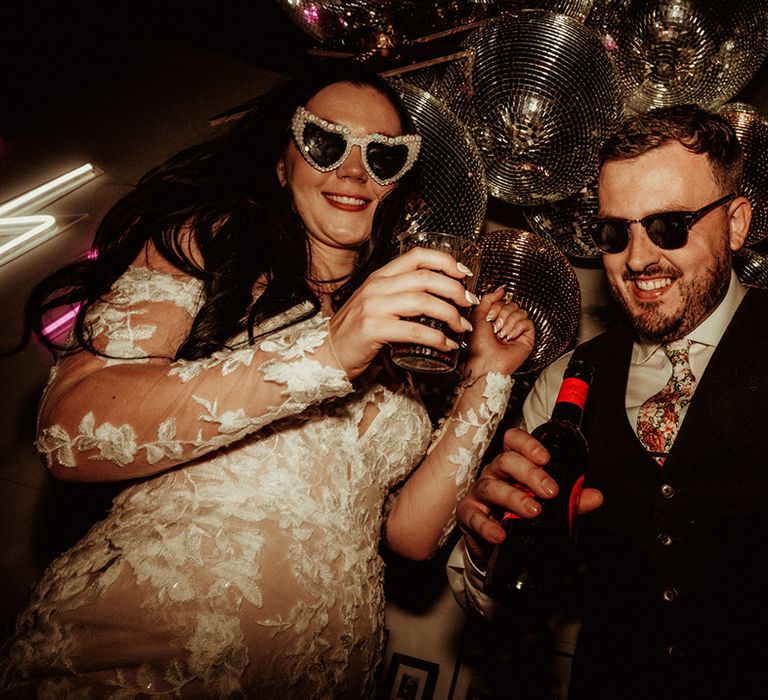 Bride and groom in wedding sunglasses dancing by large disco ball wedding decorations