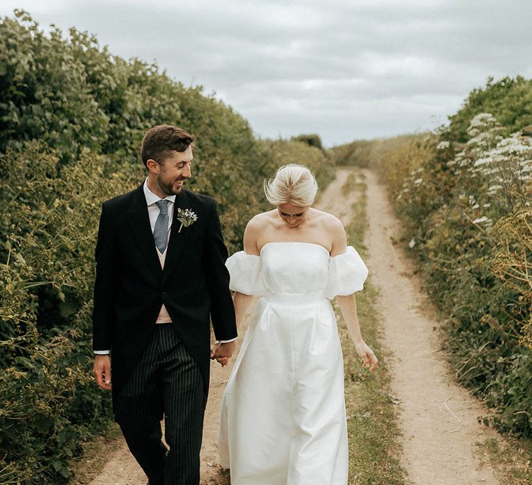 Bride in Jesus Peiro wedding dress walks alongside her groom in morning suit 