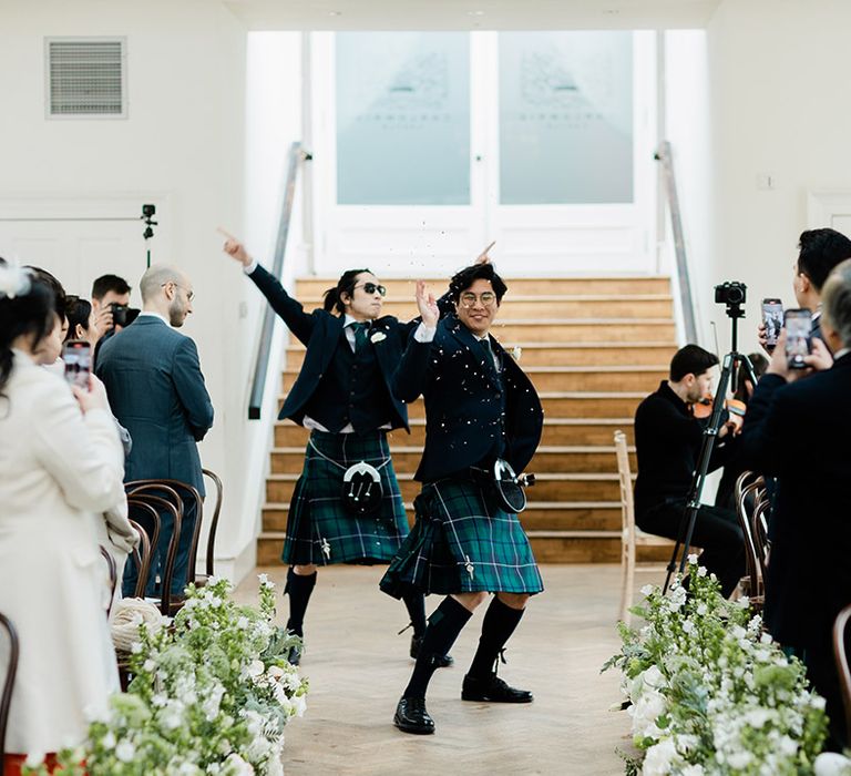 Groomsmen throw confetti whilst walking down the aisle in tartan green kilts