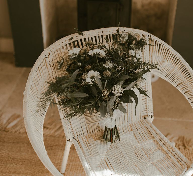 White wicker chair with a traditional white and green wedding bouquet with anemone 