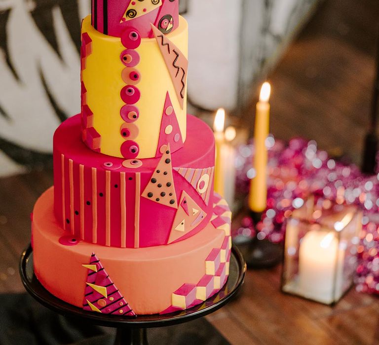 Four tiered retro wedding cake with viva magenta, custard and orange icing, triangular and alternative cake decor on black cake stand  