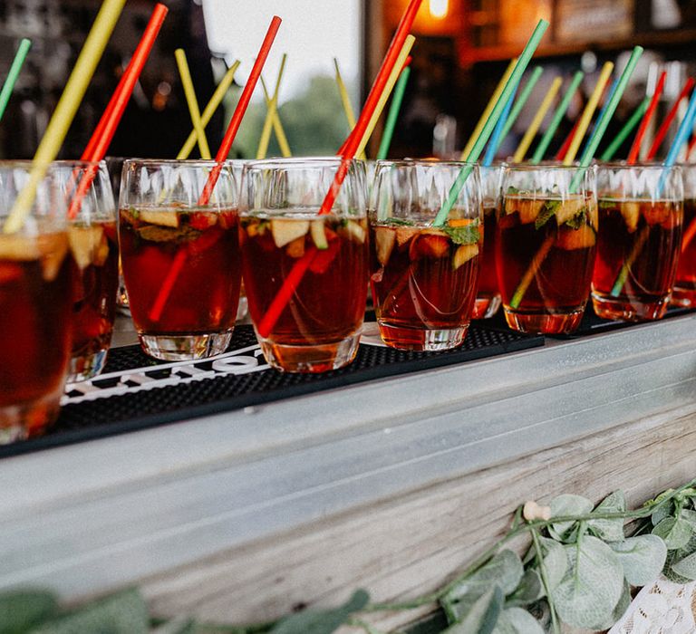 Glasses of Pimm's for the wedding guests with bright coloured paper straws 