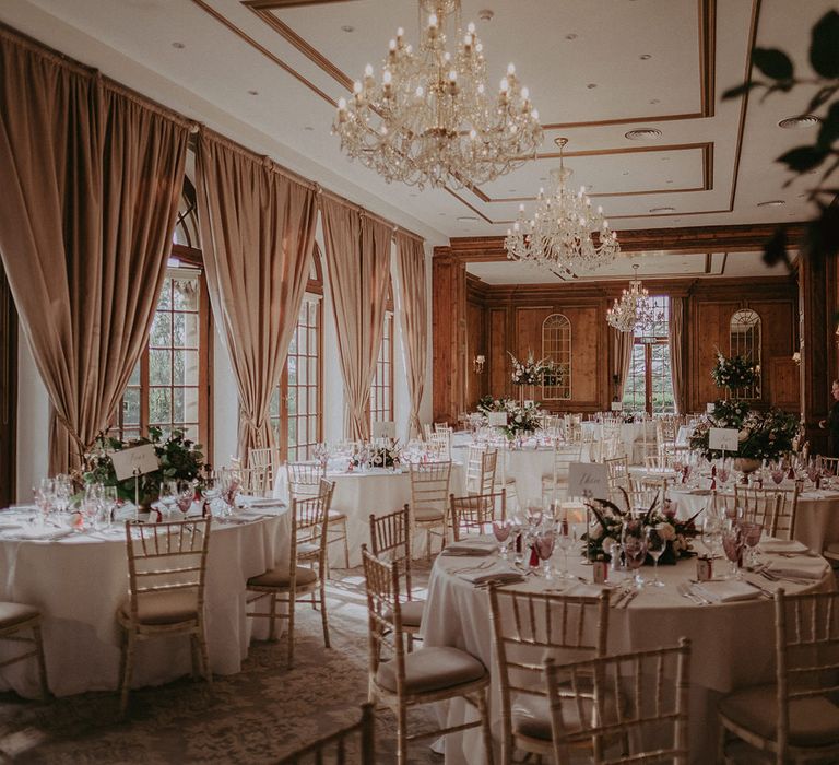 Regal styling at Hedsor House complete with round tables finished with classic floral centrepieces and chandeliers hanging from above