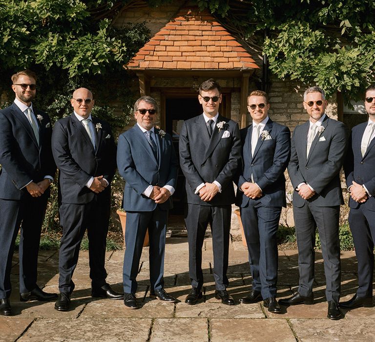 Groomsmen in navy suit with sage green ties with the groom in double breasted jacket and spotted tie all wearing sunglasses for the autumn wedding 