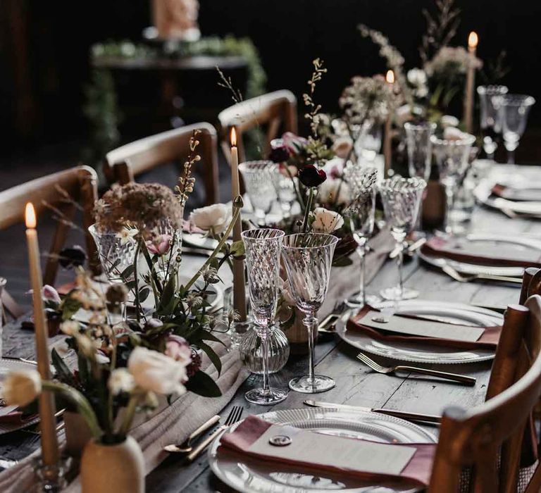 Rustic luxe wedding tablescape with white cloth table runners, foliage, baby's-breath, eucalyptus and dried flower floral arrangements, neutral tapered candles and small ceramic vases 