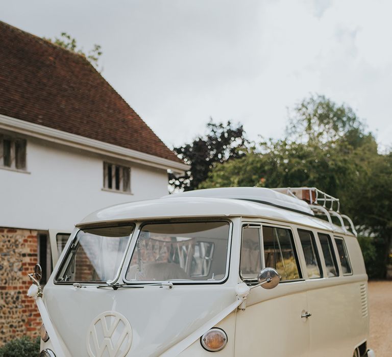 Cream VW wedding transport decorated with neutral wedding flowers and roses along the bumper of the car with white ribbon 