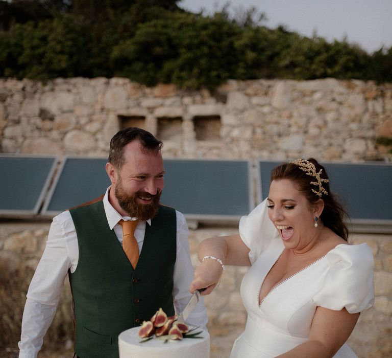 bride and groom cutting the iced wedding cake with figs during the wedding reception at private villa wedding in Greece