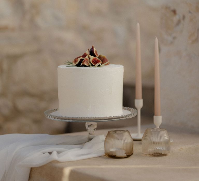 Simple iced wedding cake with figs and blush tapered candles at private villa wedding in Greece