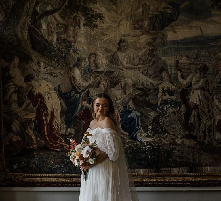 Bride in whimsical wedding dress with off the shoulder puff sleeves holding a seasonal wedding bouquet with orchids and peonies 