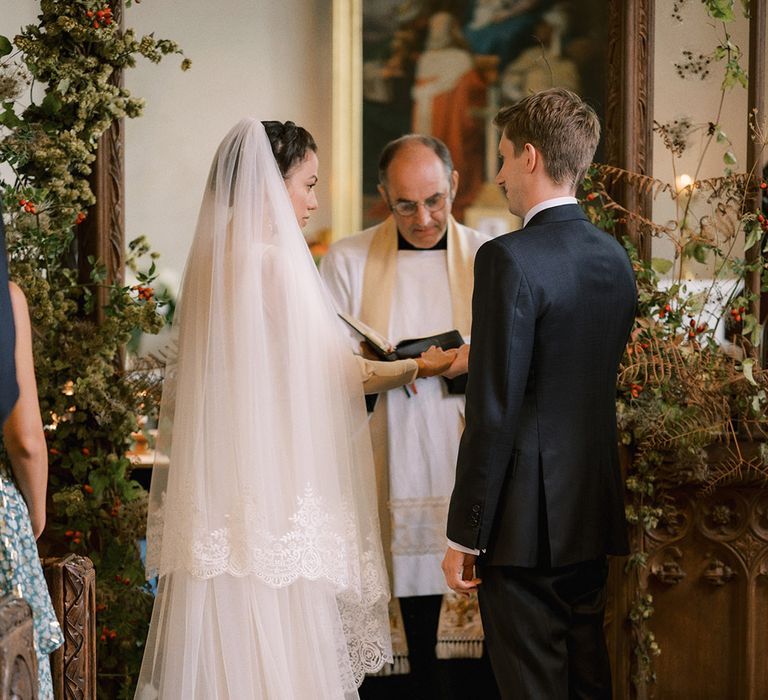 A traditional church wedding with the bride in conservative wedding dress and veil with the groom in navy suit for the ceremony 