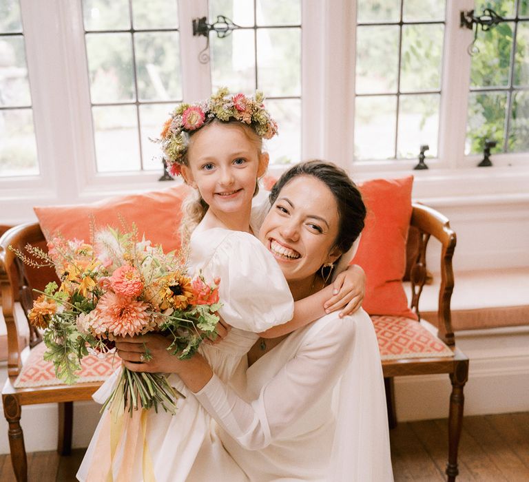 Bride hugging one of the kids attending the wedding in a white dress and colourful flower crown 