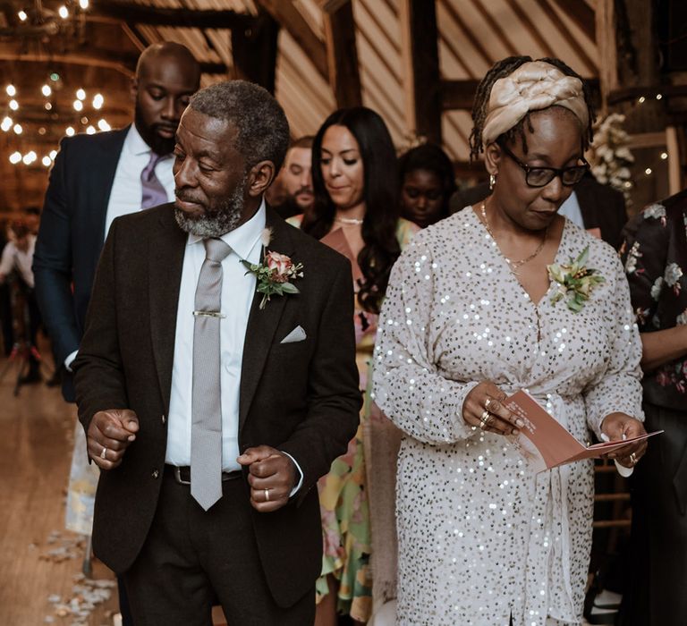 Father of the groom dancing along to the gospel choir at the ceremony with the mother of the groom in sparkly dress 