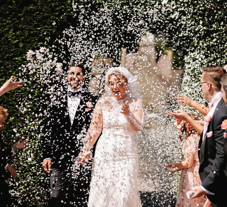 Wedding guests throw white confetti over the bride and groom at black tie luxury wedding 