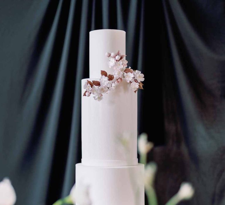 Four tier iced wedding cake with dusky pink and light pink flower decorations in front of black fabric backdrop at Settrington Orangery