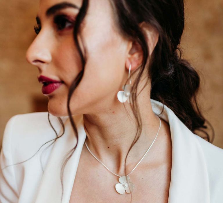 Bride in white bridal suit wearing dainty silver wedding jewellery with large flower designs at Merriscourt wedding