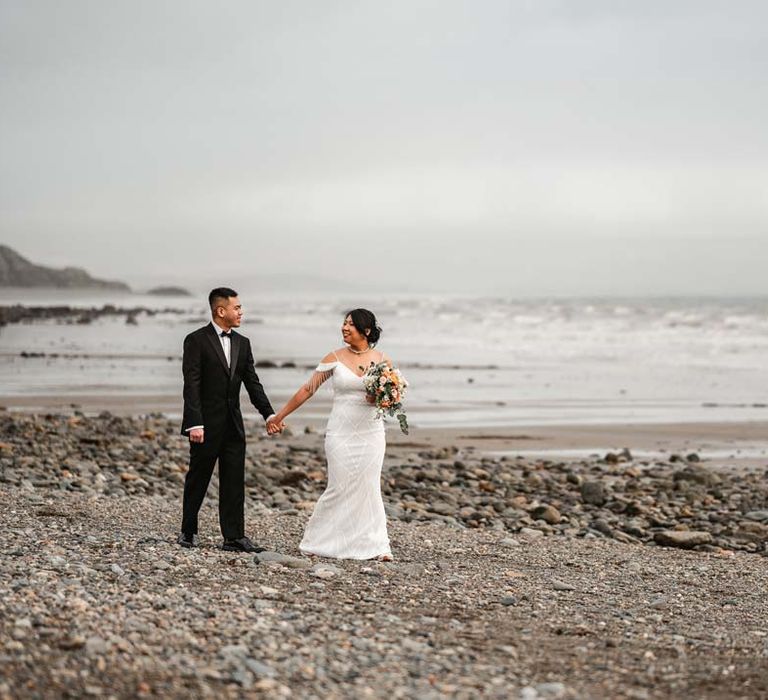 Bride and groom walking on the beach in Wales for Burmese wedding