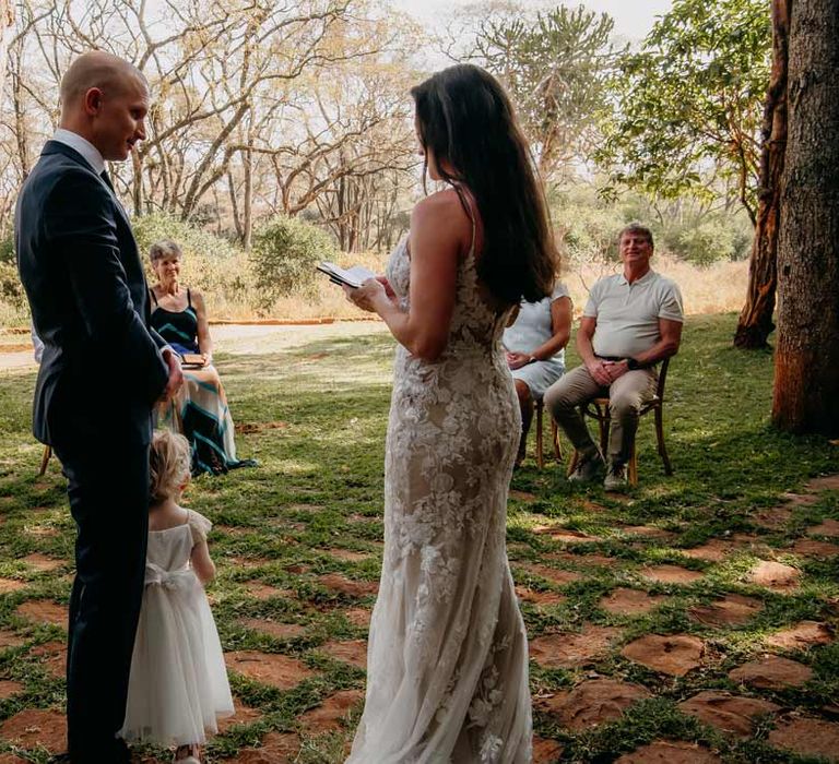 Groom in classic black grooms suit standing with bride in lace sleeveless wedding dress with puddle train at intimate elopement wedding at Giraffe Manor wedding venue Kenya