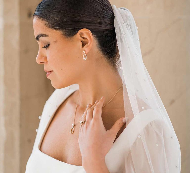 Bride in square neck wedding dress with sheer pearl embellished bridal veil and dainty silver pearl bridal jewellery 