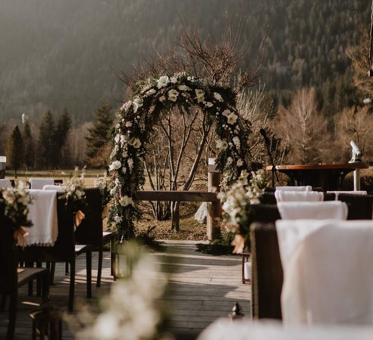 White garden rose, eucalyptus, baby's-breath and foliage wedding flower arch at outdoor wedding ceremony space at La Cabana Des Praz wedding venue in France