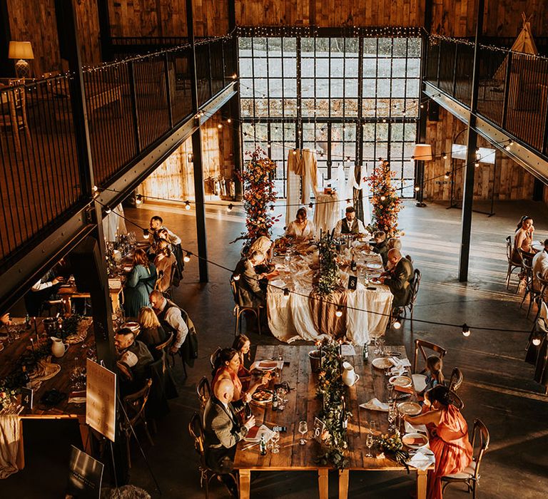 Hidden River Barns in Carlisle, Cumbria with autumnal wedding tablescape including black taper candles, festoon lighting, and leaf flower columns