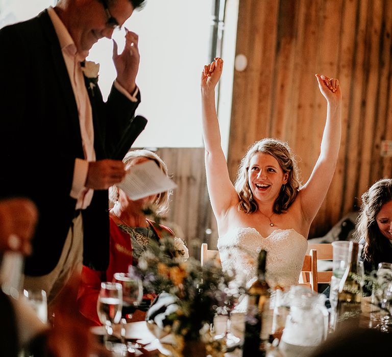 bride in a strapless lave wedding dress raising her hands in the air during the father of the bride wedding speech