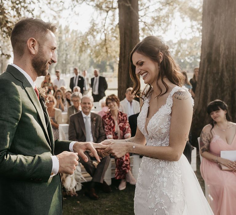 bride and groom exchange wedding rings at tenuta il cigno wedding ceremony in an appliqué wedding dress and dark green suit 