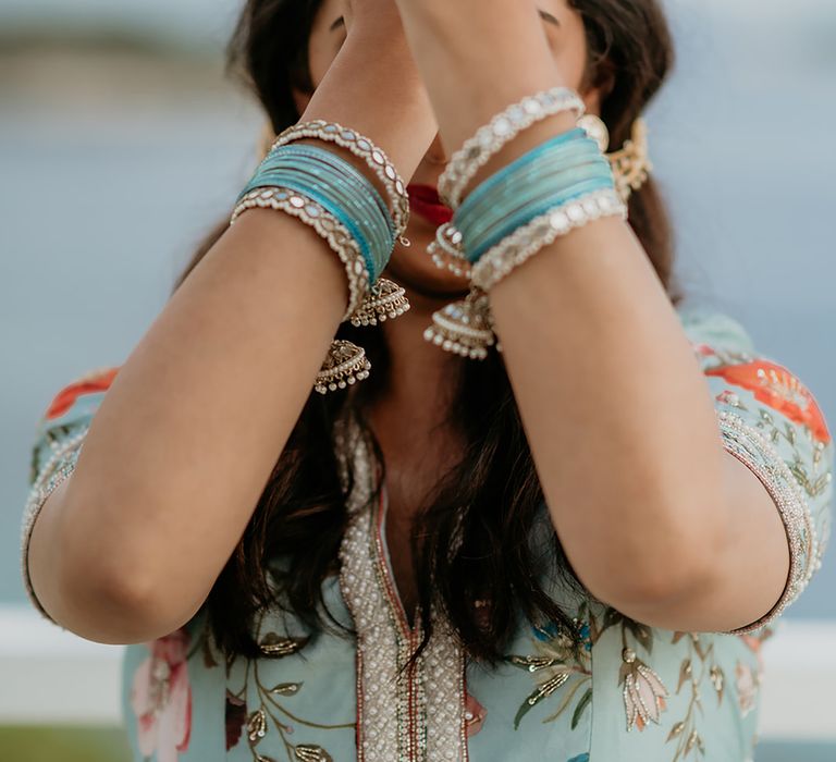 South Asian bride in turquoise traditional south asian wedding outfit shows off bridal accessories and jewelery on her wrists