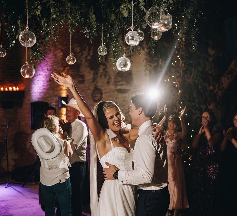 The bride and groom have their first dance together under pretty hanging lights 