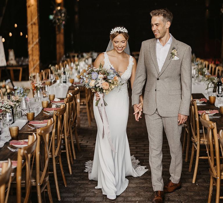 The bride carries a pastel wedding bouquet as she walks with the groom in a beige suit at wedding 