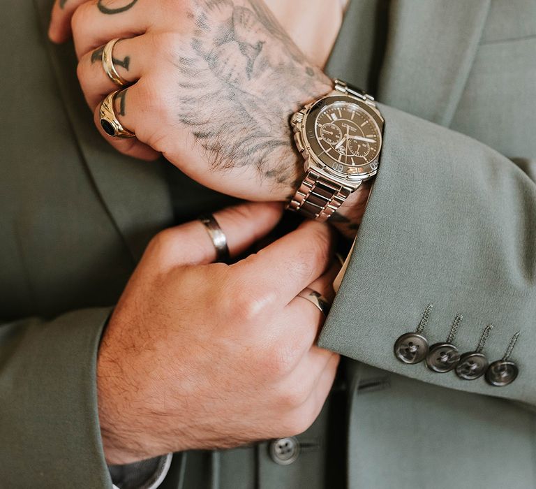 Groom in festive green suit with gold watch and rings 