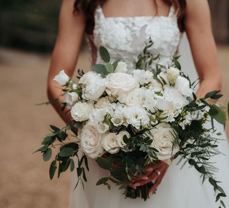 Bride carrying an all white wedding bouquet with roses and delphinium 