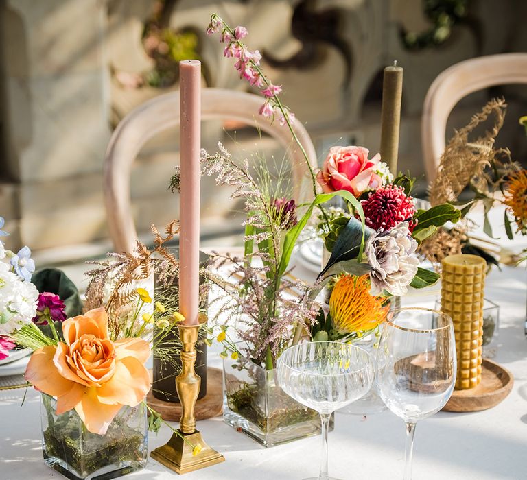 Wedding table place setting with green napkins and gold cutlery with colourful flowers in vases