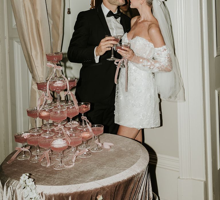 Timeless and elegant wedding reception outfits for the couple posing next to a pink champagne tower decoration 