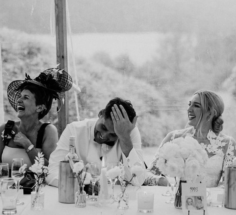 The wedding guests on the top table all laugh at the wedding speeches 