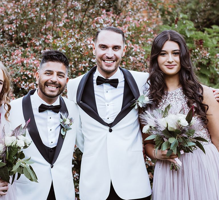 Two grooms smiling with the groomsmaids in sparkling pink bridesmaid dresses 