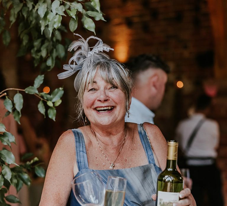 Wedding guest in blue wedding guest outfit with fascinator and glasses of wine 