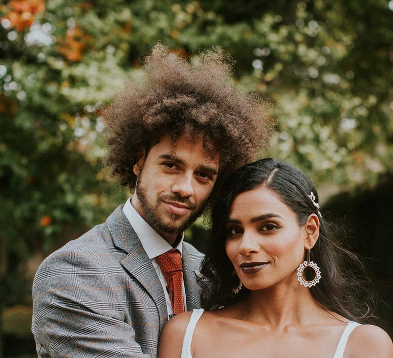 Groom in grey and orange check suit embracing his bride 