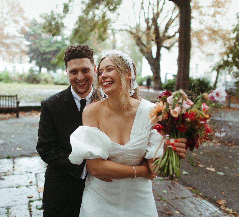 Groom embraces bride in ruched puff sleeve wedding dress with assorted bright bouquet