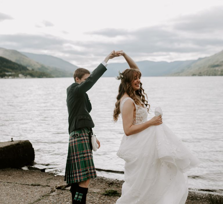 Bride with long flowing hair is spun around by her husband in traditional Scottish kilt and dress 