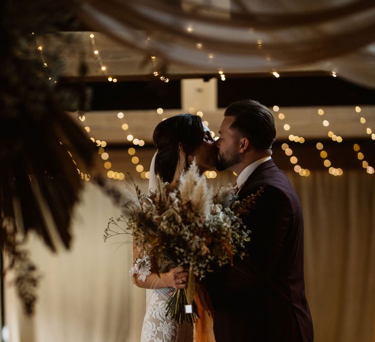 Bride in boho wedding dress and pampas grass bouquet kissing groom