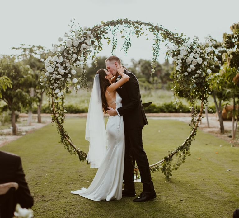 Just married at Flora Farms, Mexico in front of white flower circle altar piece