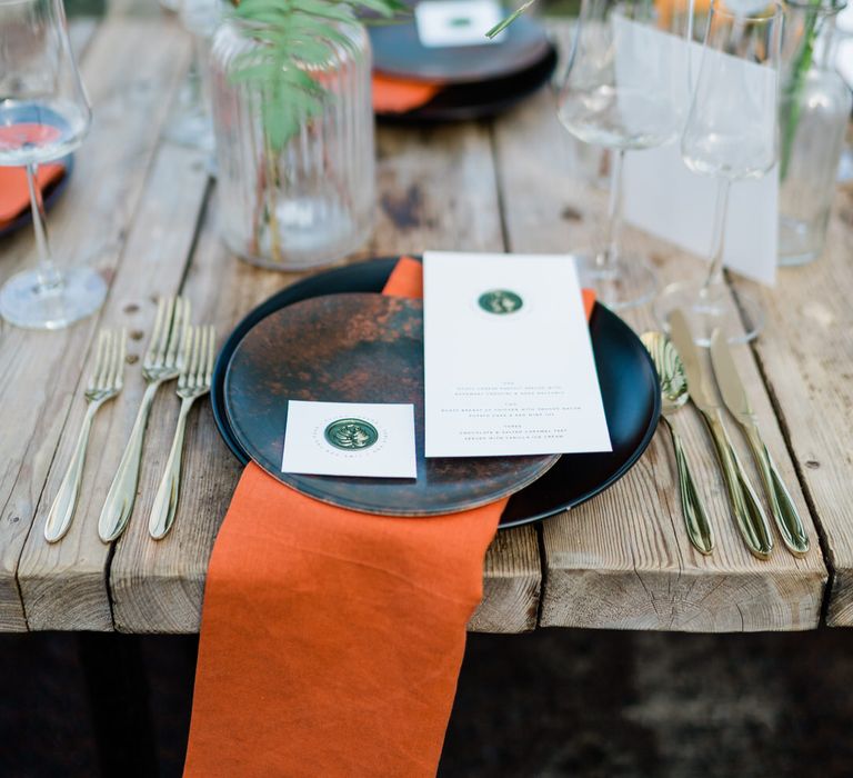 Rustic jungle wedding decor with orange napkins, jungle centrepiece and gold dinnerware