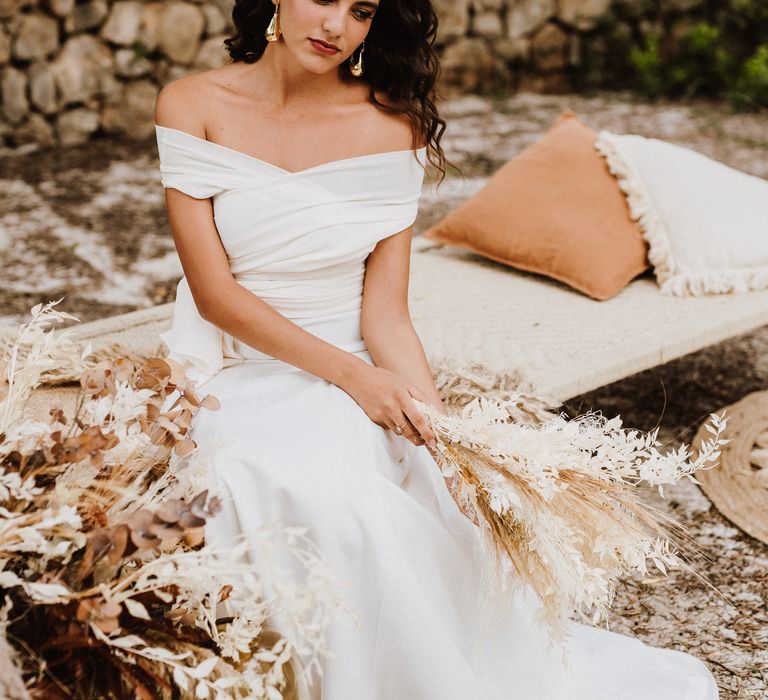 Bride sits outside on outdoor bed wearing boho gown