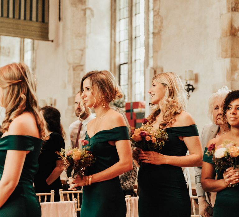 Bridesmaids in dark green off the shoulder dresses holding bouquets during the Dartington Hall wedding ceremony 