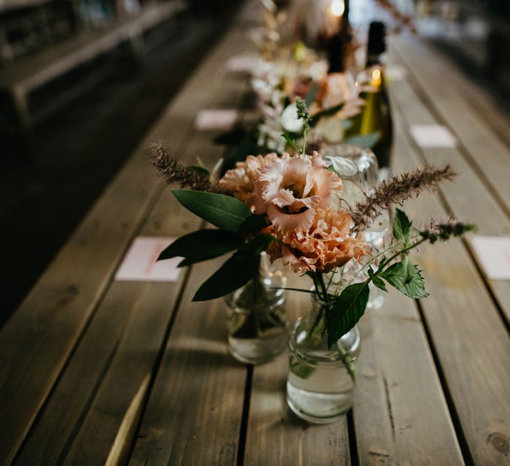 Bud vase centrepieces with peach flowers lining the centre of a trestle table